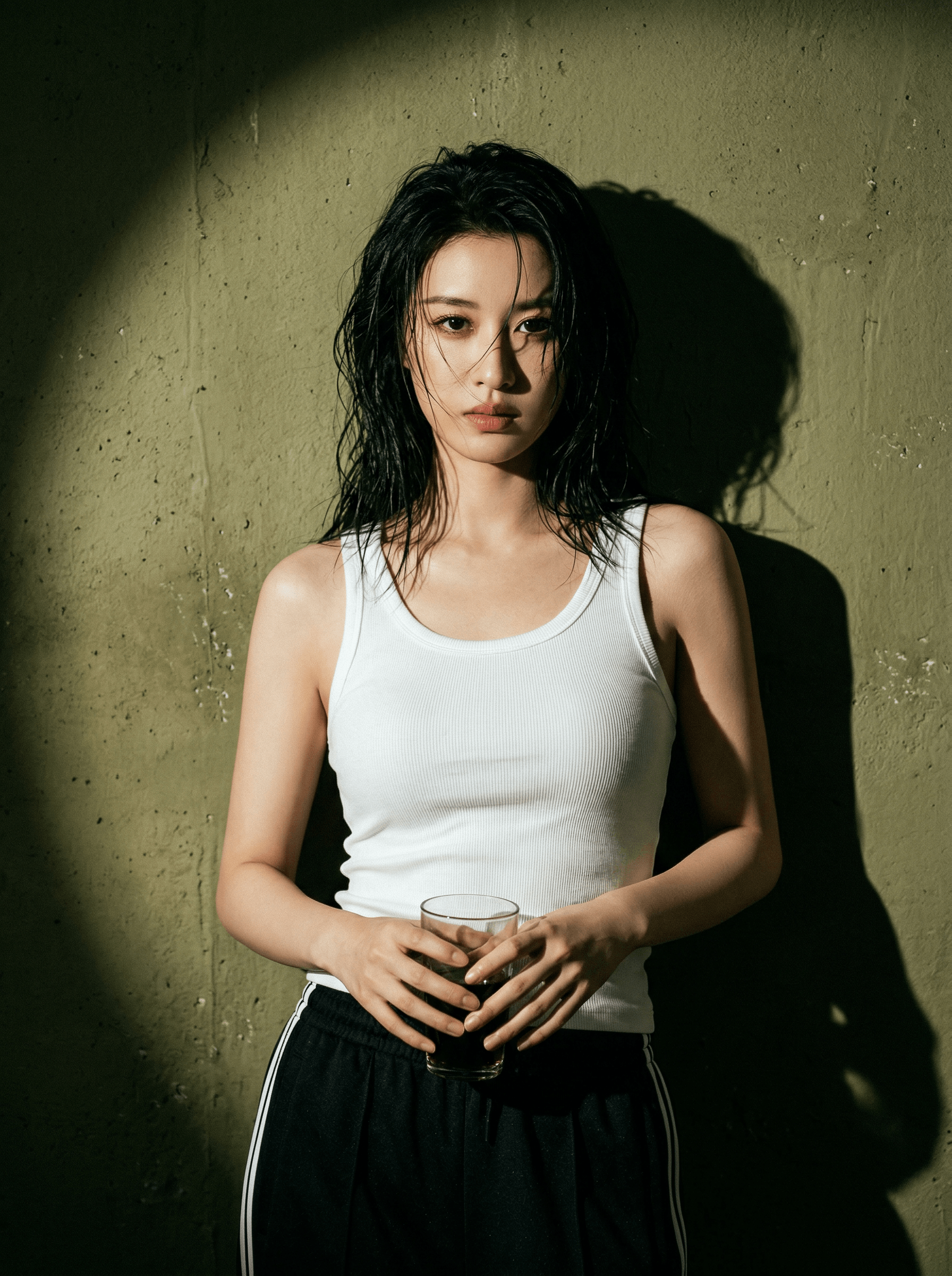Woman in a white tank top standing against a wall in a circular spotlight with a strong shadow behind her