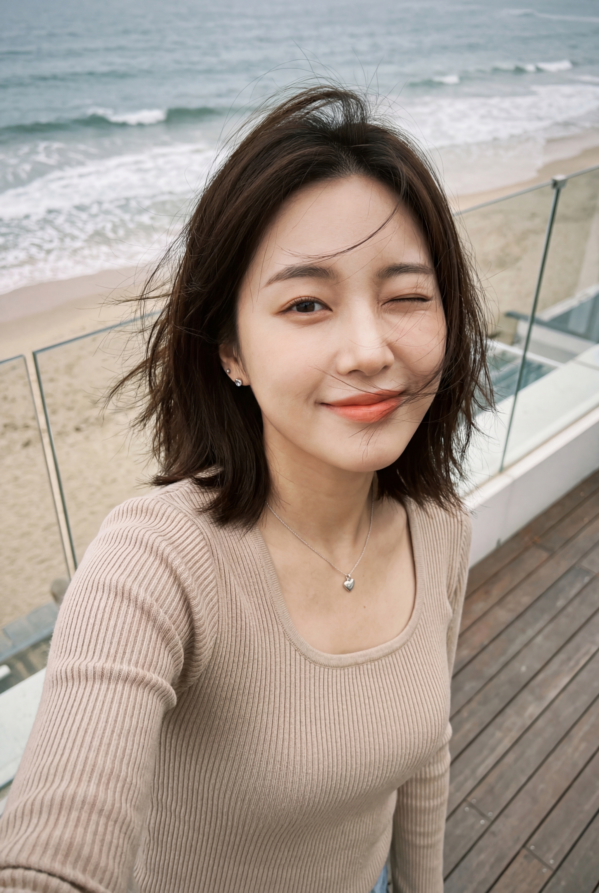 Person taking a selfie on a wooden balcony overlooking a sandy beach and ocean surf