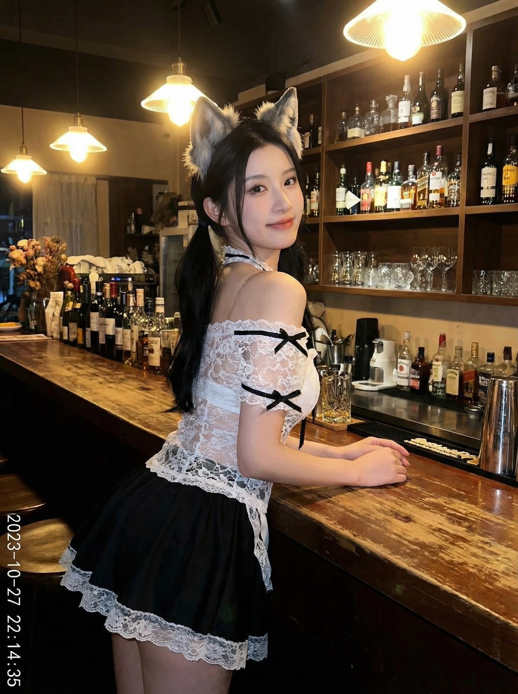 Young woman in cat-ear cosplay outfit leaning against a wooden bar counter in a warmly lit bar lined with bottles and glassware