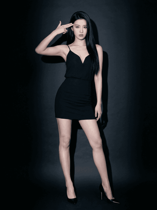 Studio portrait of a woman posing in a fitted black dress and high heels against a dark background