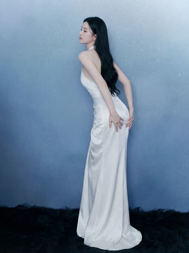 A woman with long dark hair poses in a white satin strapless gown against a blue studio backdrop