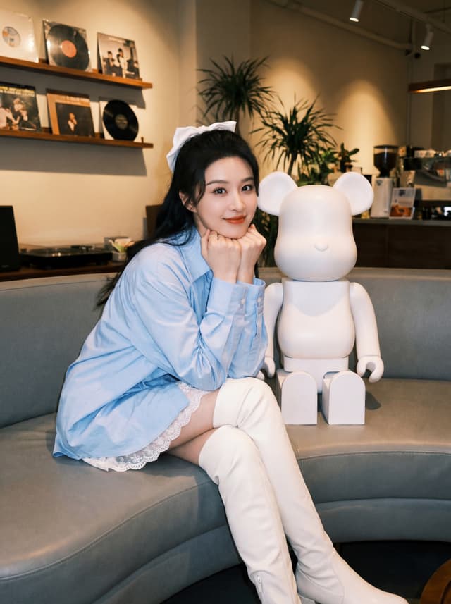 Person seated on a sofa in a modern cafe lounge next to a large Bearbrick collectible figure
