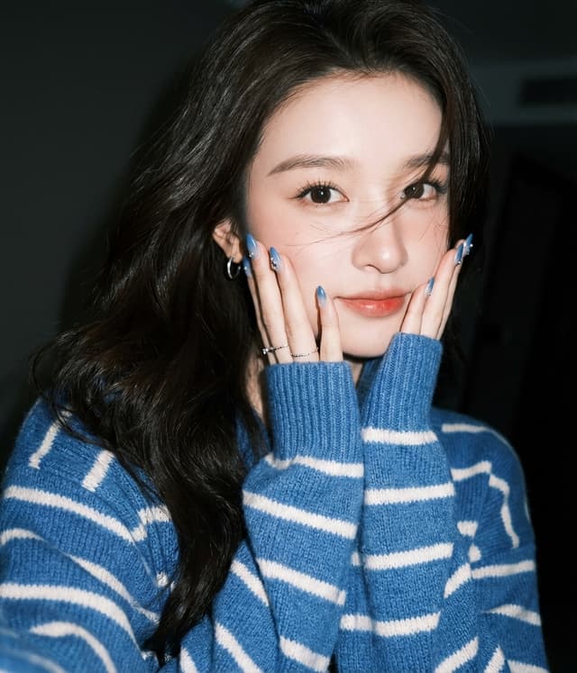 young woman in blue striped sweater posing with hands on cheeks and subtle smile