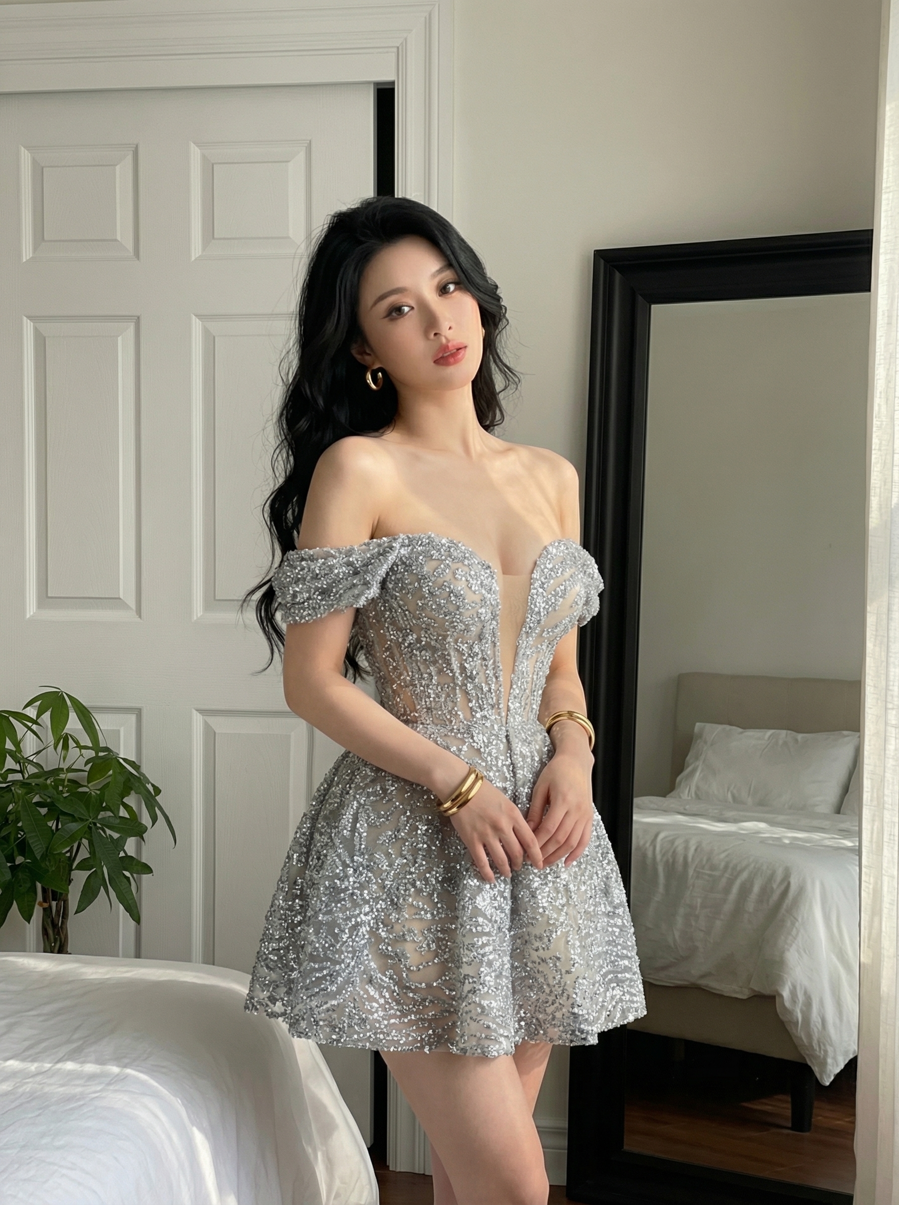 Woman in a sparkly off shoulder dress posing in a bedroom beside a full length mirror and bed